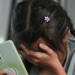 Smutna dziewczynka z telefonem w ręku, zakrywająca twarz. Czeka, aż ktoś do niej napisze.