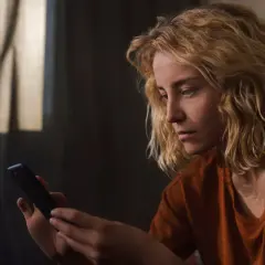 Zamyślona dziewczyna z blond włosami trzyma telefon, czekając na wiadomość. Może ta dziewczyna nie odpisuje.