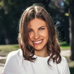 Uśmiechnięta brunetka w białej koszulce, idealna do zadawania pytań do nowo poznanej osoby.