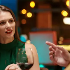 Kobieta w zielonej sukience i mężczyzna rozmawiają przy winie. Czy to przykład, czego nie robić na pierwszej randce?