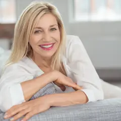 Uśmiechnięta blondynka na kanapie. Jej spojrzenie i uśmiech to najlepszy dowód, jak komplementować kobietę.