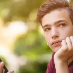 Chłopak z telefonem i słuchawkami zastanawia się, o czym rozmawiać z dziewczyną przez telefon.