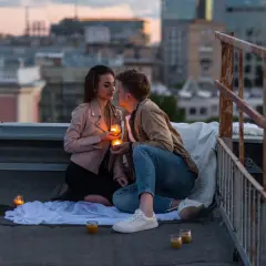Romantyczny wieczór na dachu. Para trzyma świece, patrząc sobie w oczy. Czy napisać pierwsza do faceta?