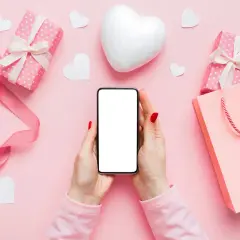 Dłonie trzymają telefon, otoczone prezentami i serduszkami. Idealne tło do pisania długich miłosnych smsów dla niej.