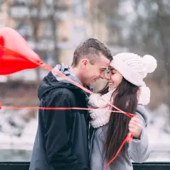 Para wzruszona, trzymająca czerwone balony w kształcie serca. Chłopak szepcze jej do ucha, co napisać dziewczynie żeby się wzruszyła.