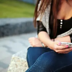 Dziewczyna z różowym lakierem na paznokciach pisze sms-a, zastanawiając się, jak wkręcić chłopaka przez sms.