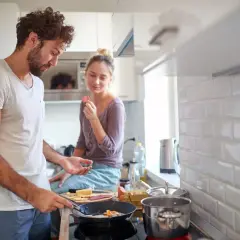 Para, który gotuje śniadanie, gdy facet proponuje wspólne mieszkanie. Ona je coś z ręki, on smaży jajka.