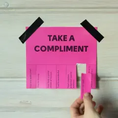 Różowa kartka z napisem "TAKE A COMPLIMENT" i odrywanymi kuponami z pochwałami. Daje to pomysł na inteligentne odpowiedzi na komplementy.