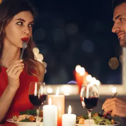 Romantyczna kolacja przy świecach. Ona w czerwonej sukience, on w białej koszuli. Widać, jak flirtować, patrząc na siebie nawzajem.