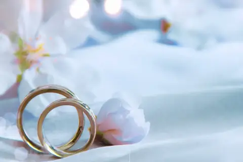 Dwa złote obrączki na tle delikatnych kwiatów i jasnego materiału. Dziękuję Ci, mój kochany, za bycie razem.