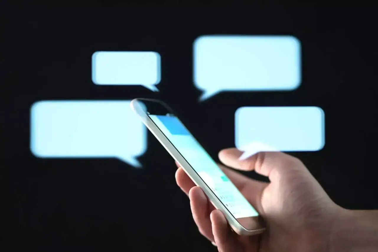 Dłoń trzyma smartfon, a wokół unoszą się dymki czatu. Czy to znak, że ktoś stosuje ghosting? Co to znaczy, gdy rozmowa nagle milknie?