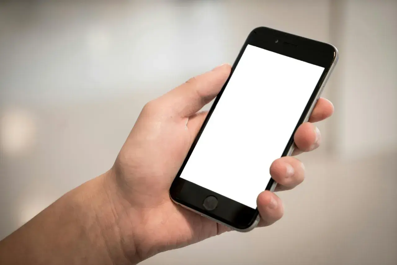 Dłoń trzyma smartfon z pustym ekranem, idealny do pokazania szybkich odpowiedzi SMS, przykładów komunikacji.