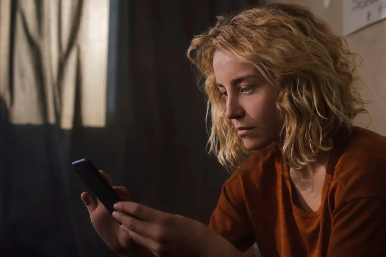 Zamyślona dziewczyna z blond włosami trzyma telefon, czekając na wiadomość. Może ta dziewczyna nie odpisuje.