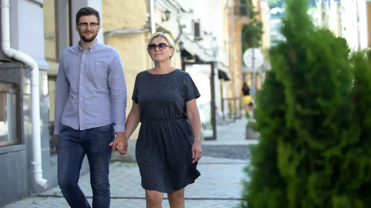 Para spaceruje ulicą, trzymając się za ręce. Młodszy mężczyzna w okularach i starsza kobieta pokazują, że różnica wieku w związku nie jest przeszkodą.