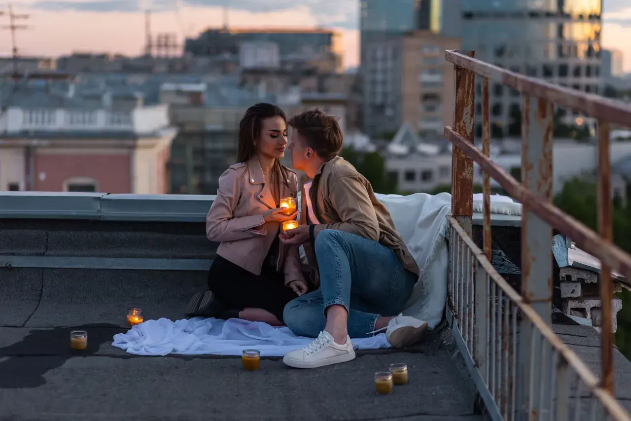 Romantyczny wieczór na dachu. Para trzyma świece, patrząc sobie w oczy. Czy napisać pierwsza do faceta?