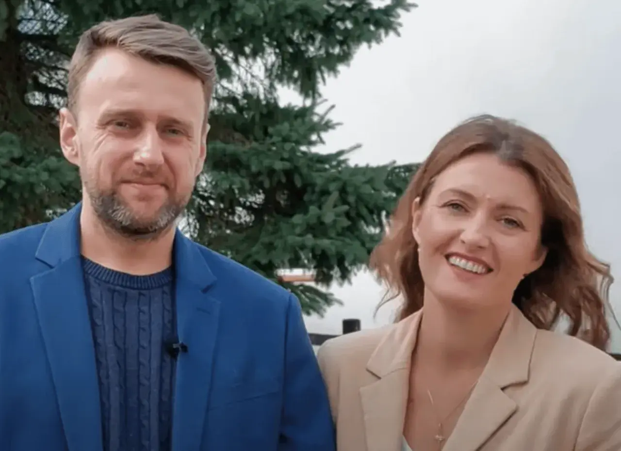 Uśmiechnięta para, on w niebieskiej marynarce, ona – żona z Ukrainy – w beżowej.