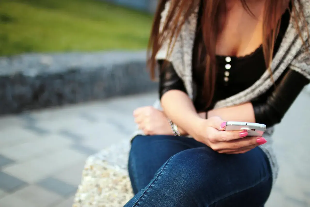 Dziewczyna z różowym lakierem na paznokciach pisze sms-a, zastanawiając się, jak wkręcić chłopaka przez sms.